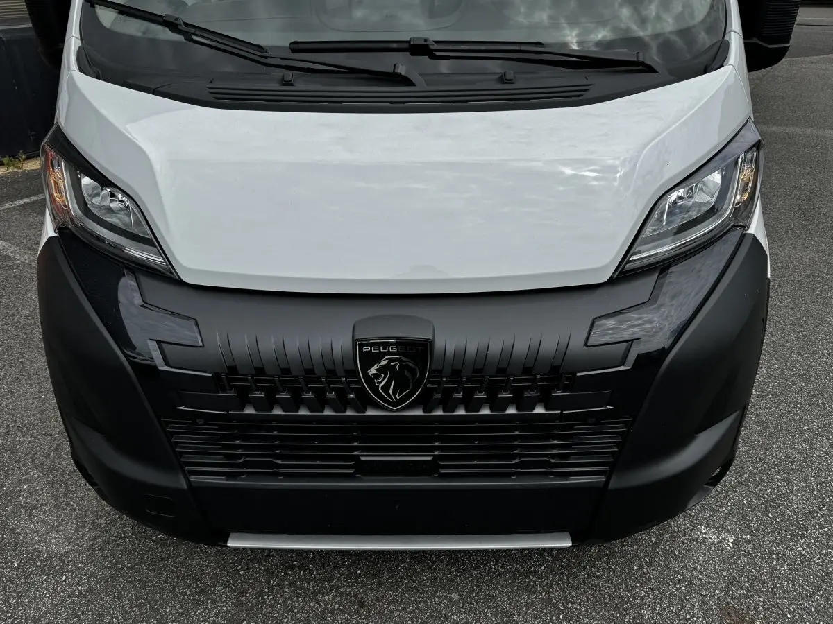 Vue frontale rapprochée du Peugeot Boxer Fourgon blanc avec calandre noire et logo lion central visible.