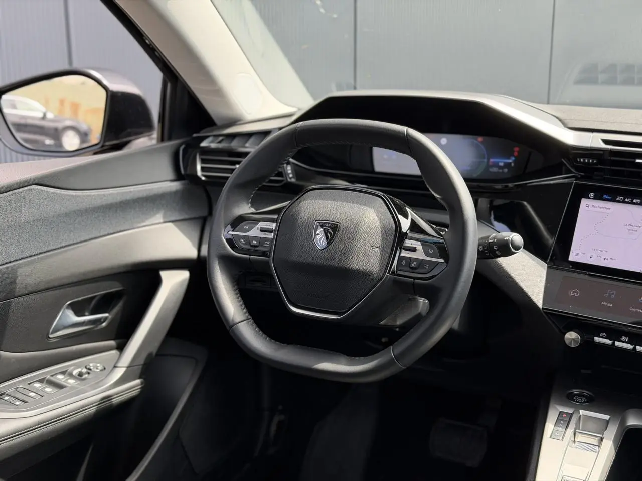 Vue intérieure centrée sur le volant cuir noir de la Peugeot 308 Hybrid 2025 avec écran tactile et commandes intégrées.