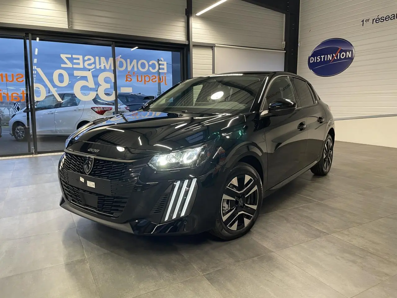 Peugeot 208 noir métallisé vue 3/4 avant droit en intérieur, avec feux LED et jantes alliage bi-ton.