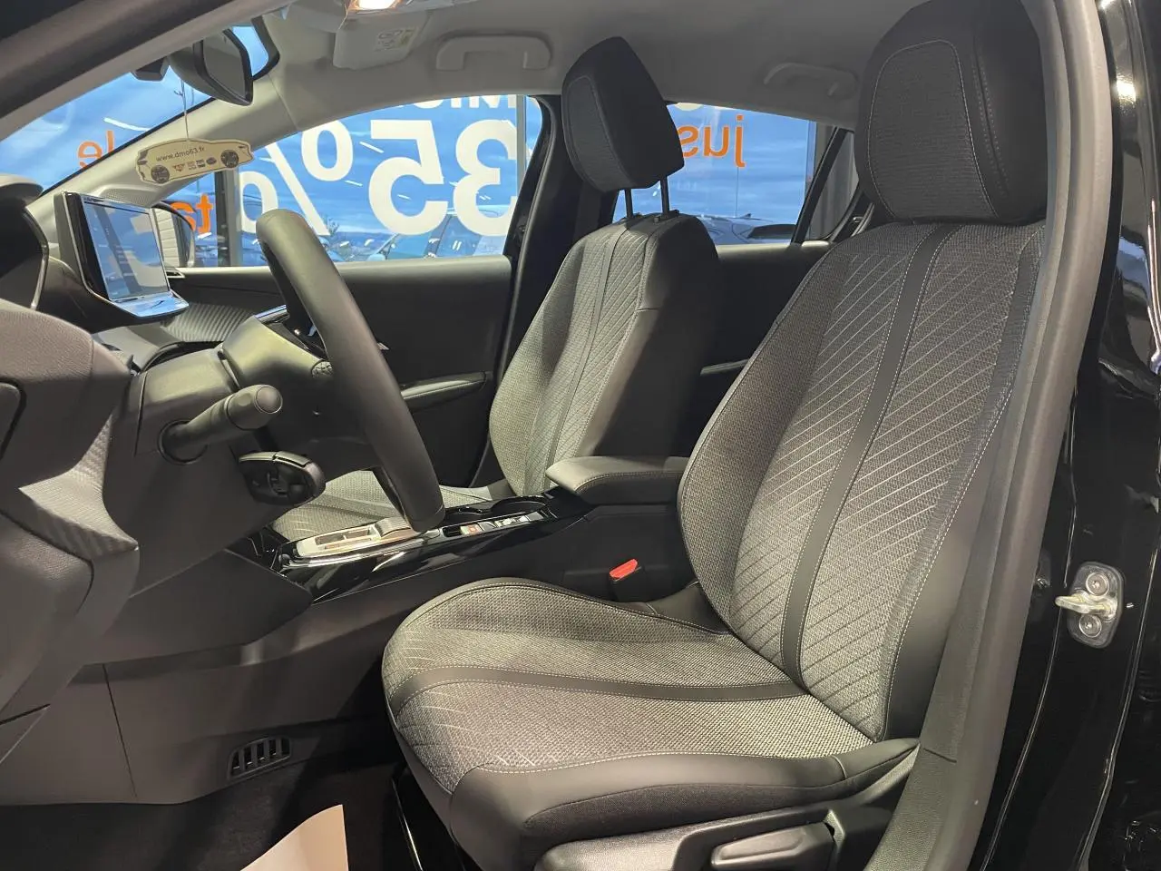 Vue intérieure côté conducteur de la Peugeot 208 noire métallisée, sièges tissu gris avec surpiqûres Quartz et volant cuir.
