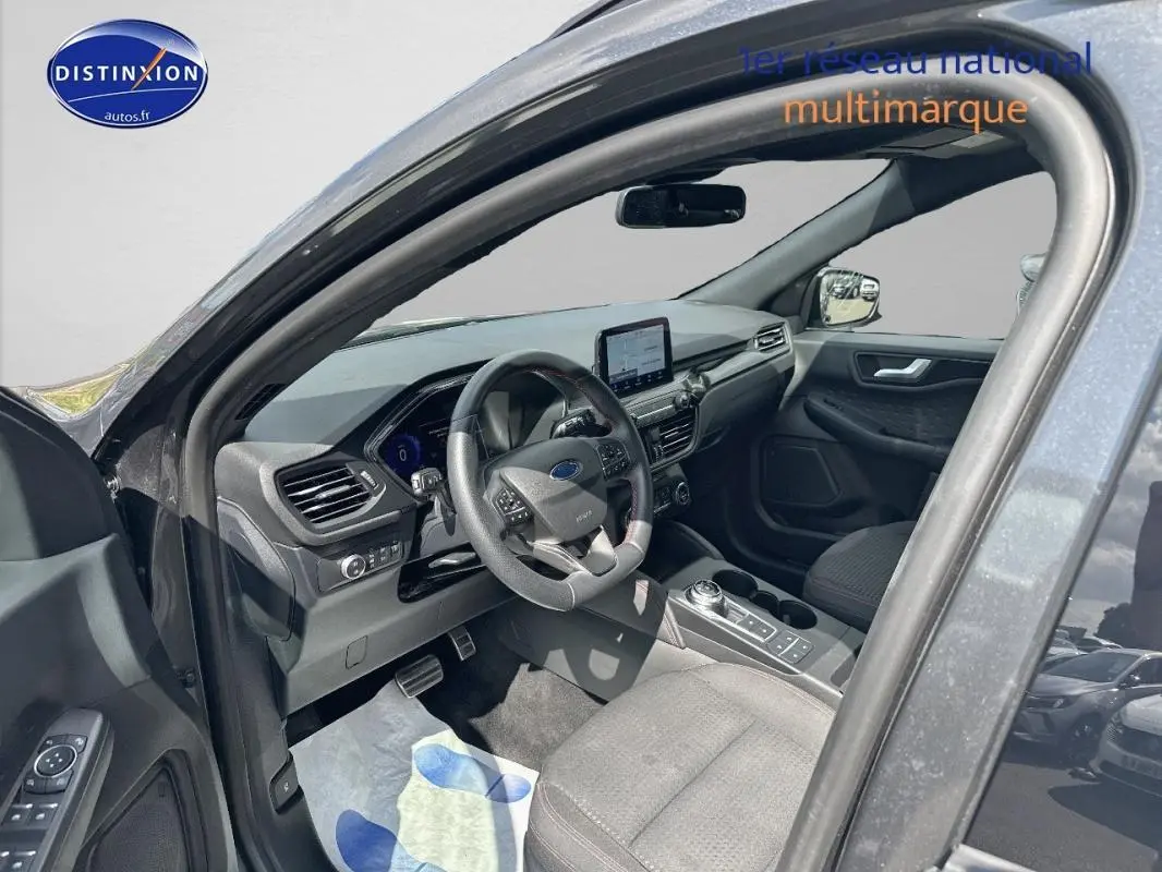 Intérieur gris foncé du Ford Kuga 2022 vu côté conducteur, avec tableau de bord moderne et écran tactile central.