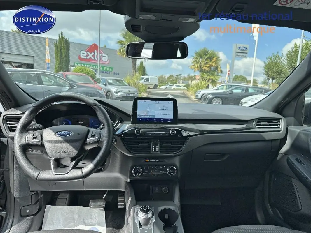 Vue intérieure avant du Ford Kuga 2022 gris foncé, montrant le tableau de bord avec écran tactile et volant multifonction.