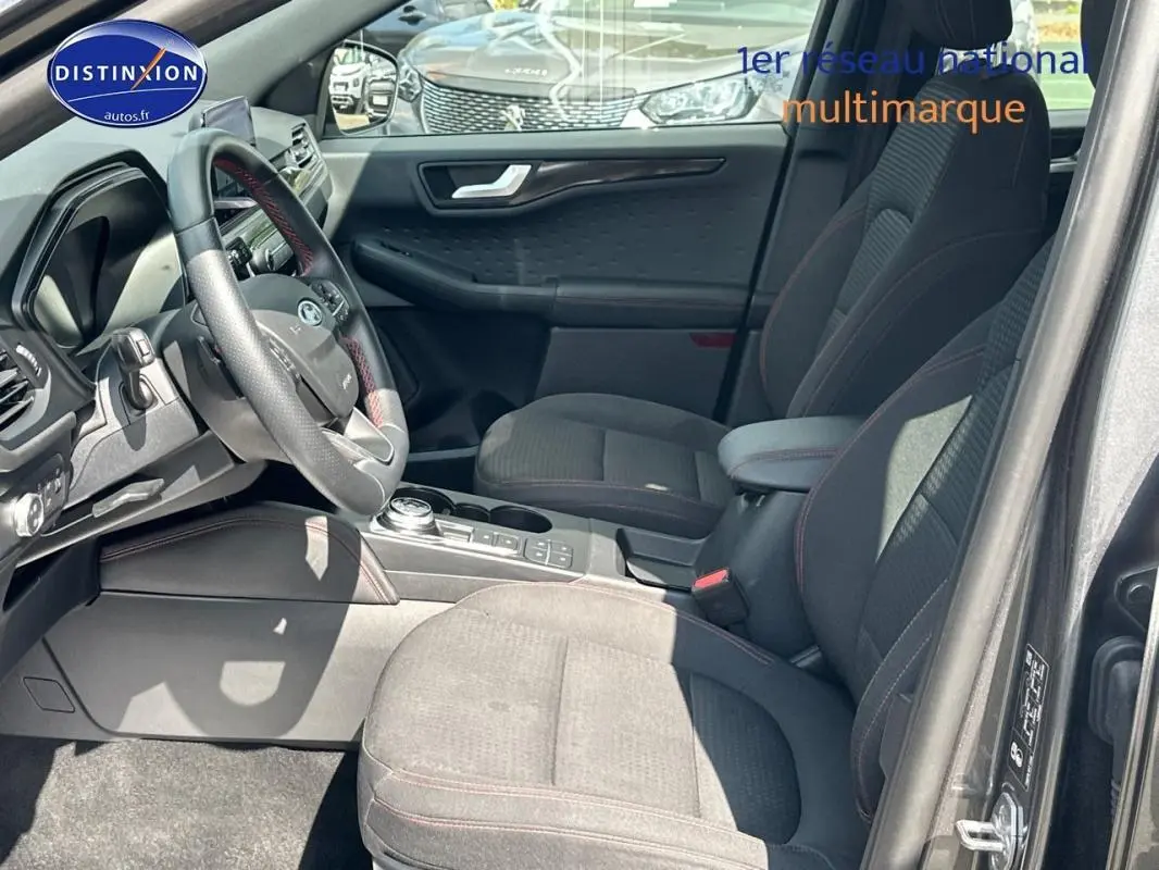 Vue intérieure côté conducteur du Ford Kuga gris foncé 2022, avec sièges sport et volant cuir à surpiqûres rouges.