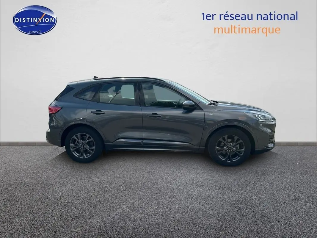 Ford Kuga gris foncé vu de profil côté gauche, avec jantes alliage 18 pouces et barres de toit visibles.