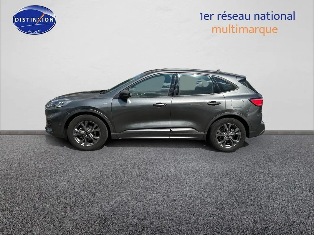 Ford Kuga gris foncé vue de profil côté gauche, avec jantes alliage 18 pouces et barres de toit visibles.