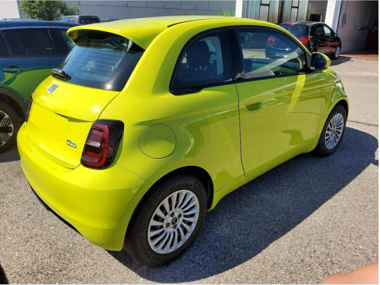 Fiat 500 électrique jaune Acid vue 3/4 arrière côté droit, avec feux arrière foncés et jantes blanches.