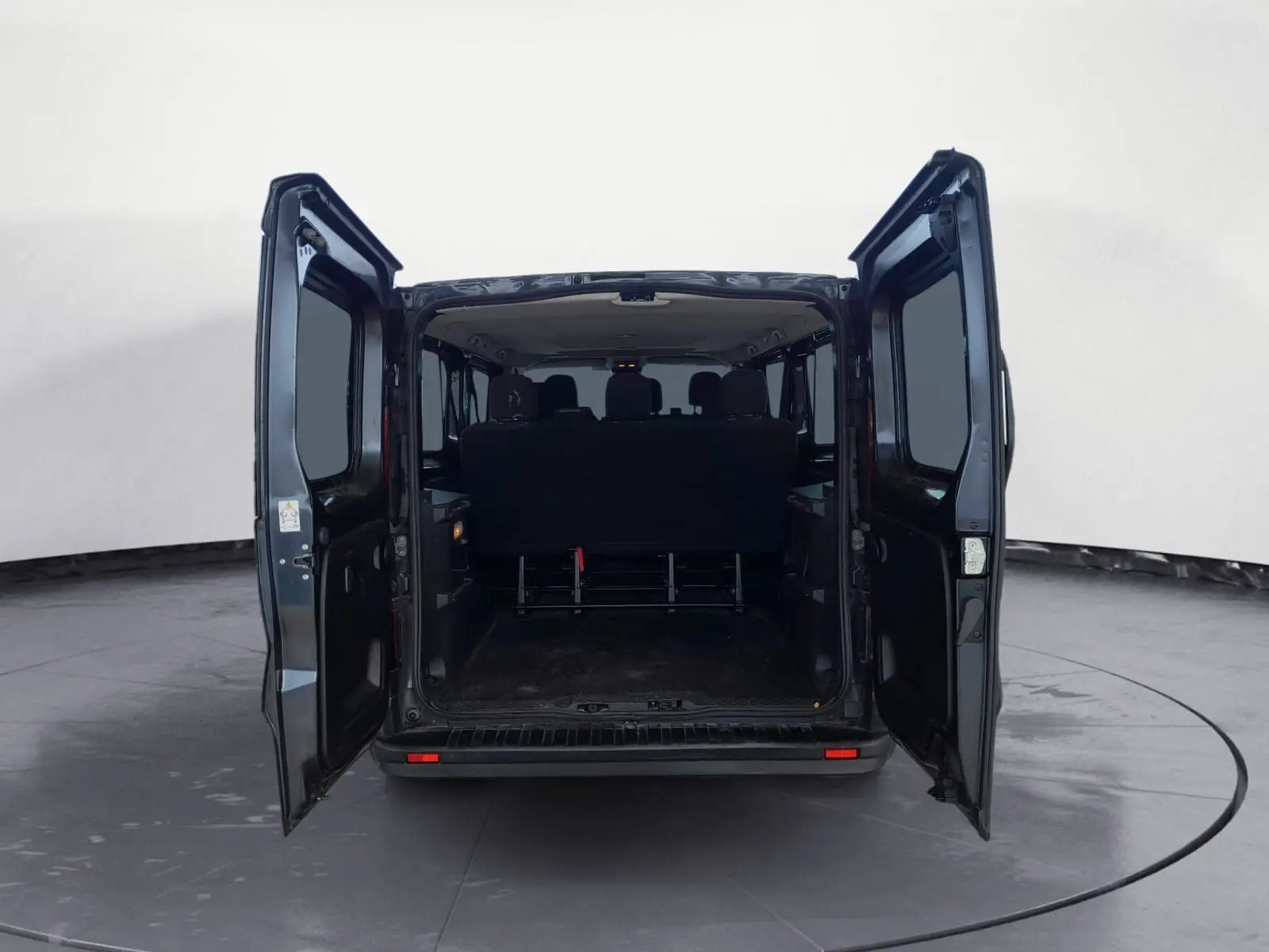 Vue arrière du Renault Trafic Combi gris foncé métal avec portes ouvertes dévoilant l'espace intérieur et les sièges passagers.
