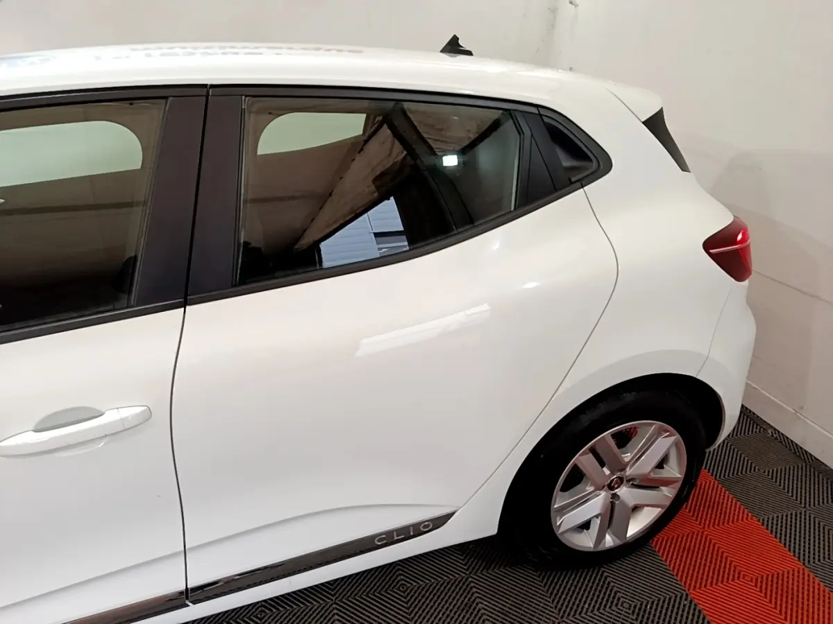 Vue latérale côté droit d'une Renault Clio blanche avec jante alliage et logo Clio sur la bas de porte.