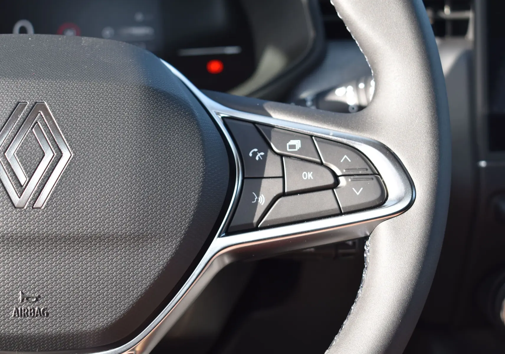 Gros plan sur la partie droite du volant noir de la Renault Clio V 2025, avec commandes multifonctions et logo Renault visible.