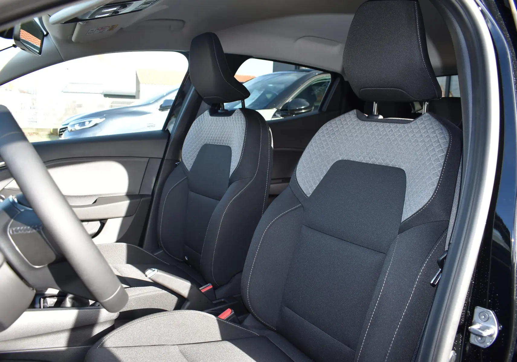 Vue intérieure côté conducteur de la Renault Clio V TCE 90 noire, mettant en valeur les sièges avant bicolores gris et noir.