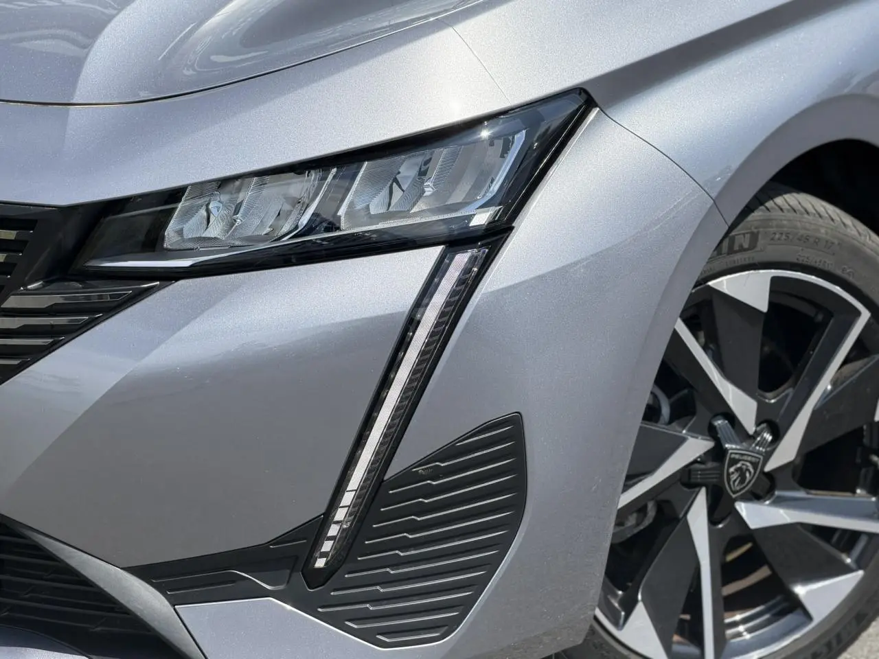 Gros plan sur l'avant droit gris Artense du Peugeot 308 Hybrid 145, mettant en valeur le phare LED et la jante alliage 17 pouces.