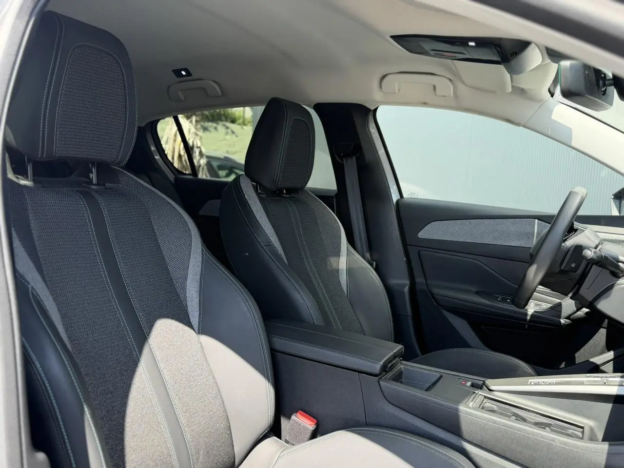 Vue intérieure côté conducteur de la Peugeot 308 Hybrid gris Artense, sièges tri matières avec surpiqûres bleues et accoudoir central.