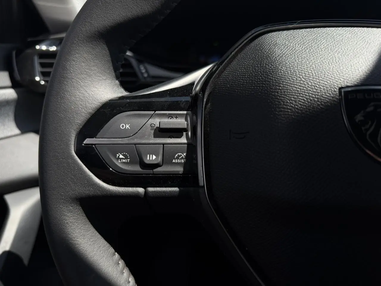 Gros plan sur le volant noir de la Peugeot 308 Hybrid 2025, avec commandes intégrées côté gauche et logo lion visible.