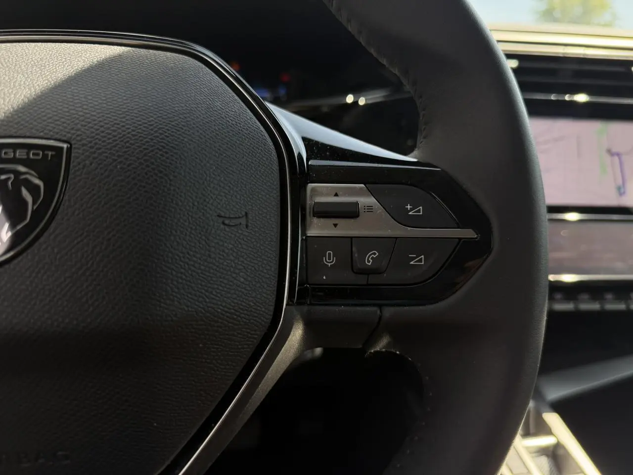 Gros plan sur le côté droit du volant cuir Peugeot 308 Hybrid 2025 avec commandes intégrées et écran tactile en arrière-plan.