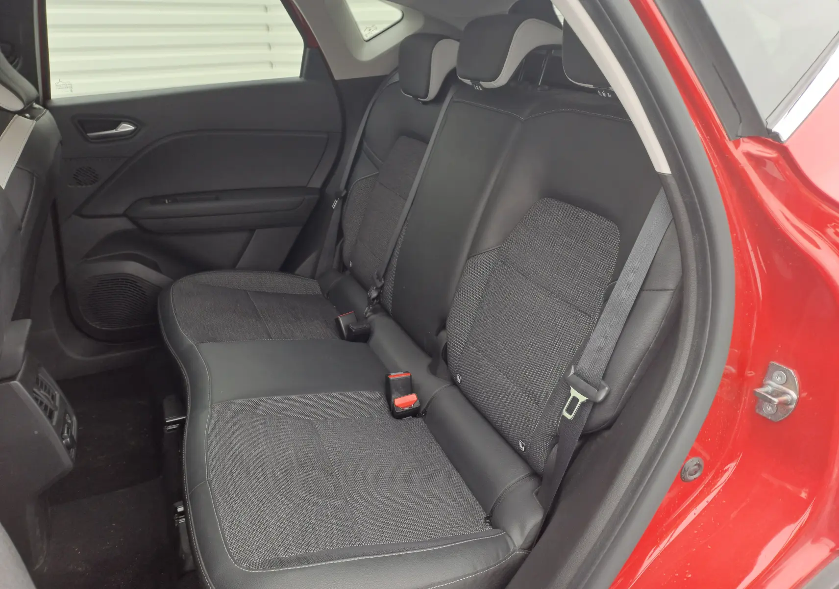 Vue intérieure du siège arrière droit du Renault Captur rouge flamme métal 2024 avec sellerie noire mixte cuir et tissu.
