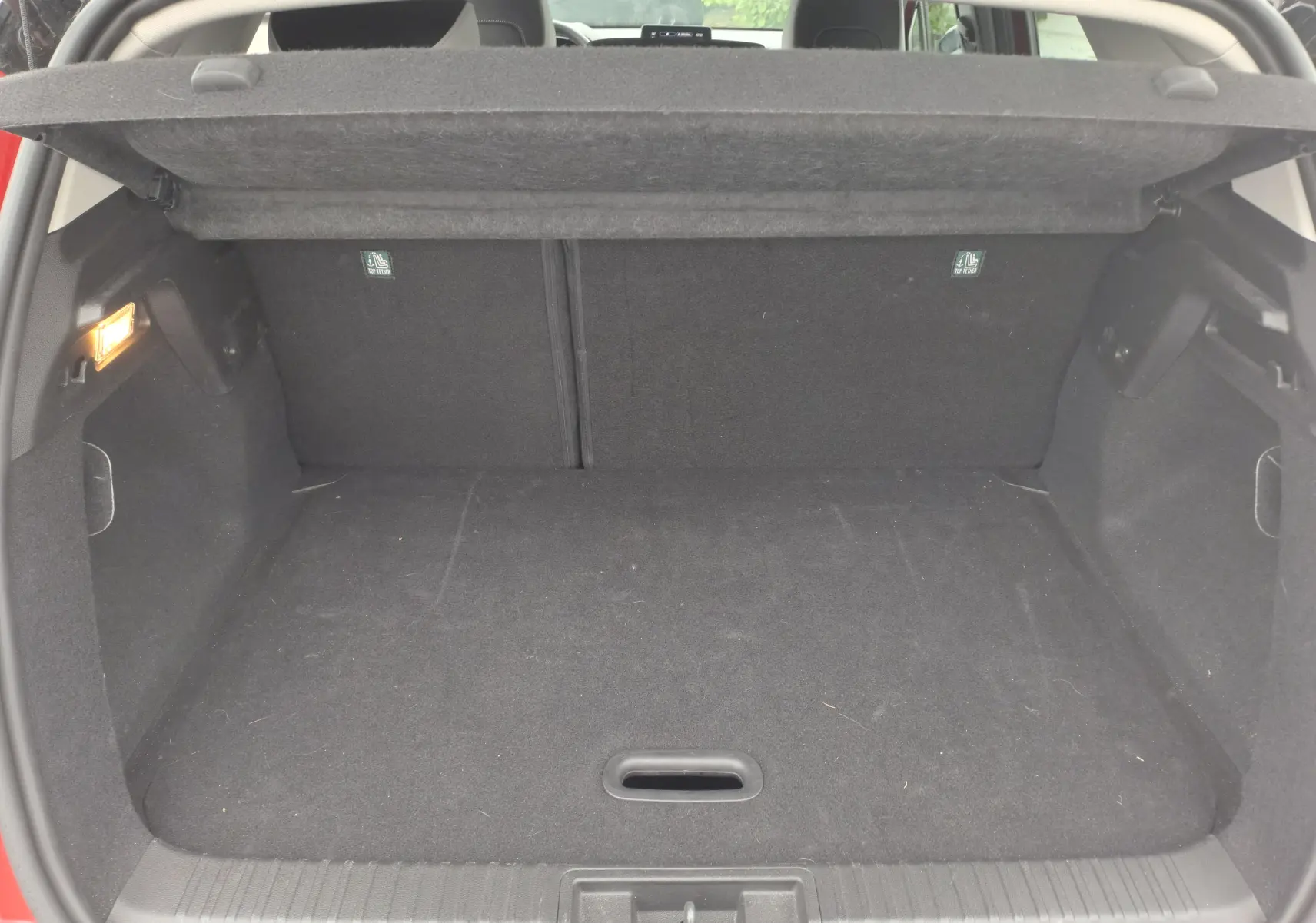 Coffre ouvert vu de l'arrière d'un Renault Captur TCE 90CH TECHNO rouge flamme, espace de chargement vide et tapis noir.