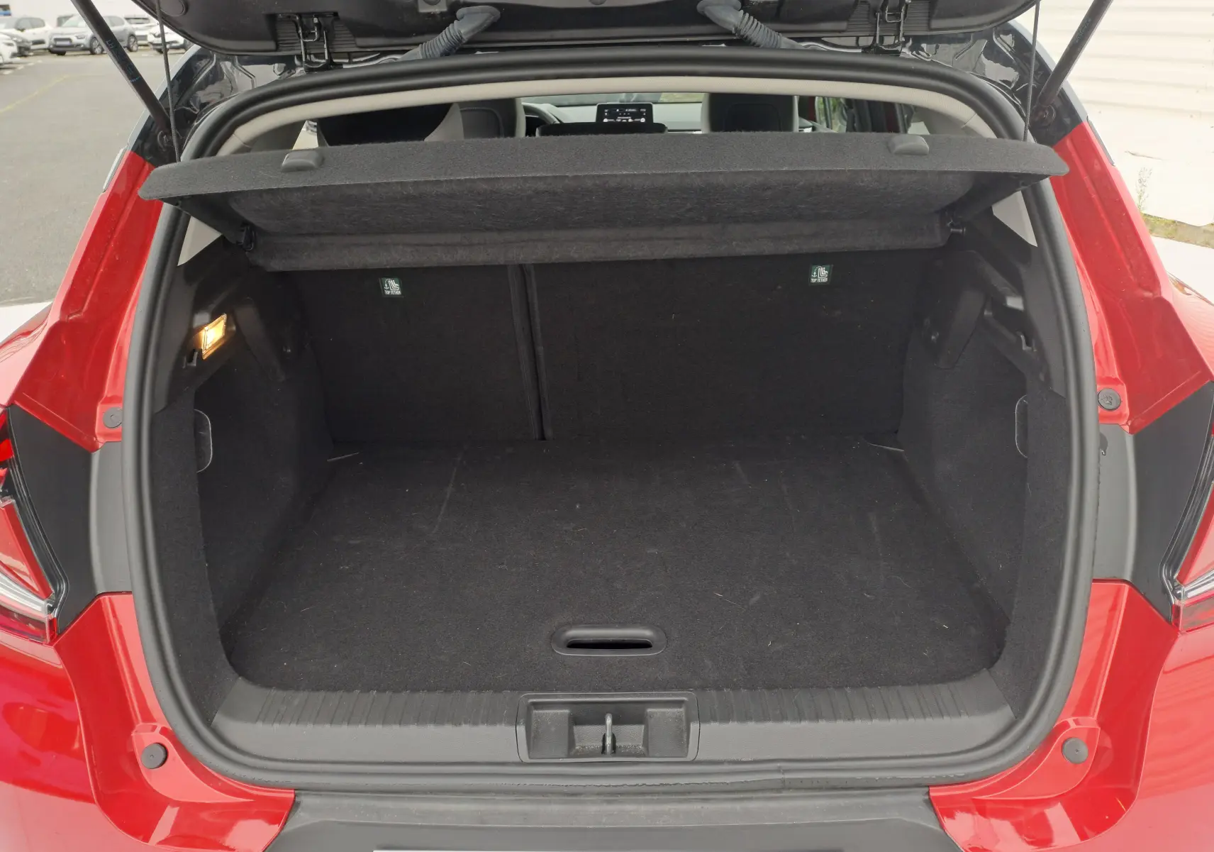 Coffre ouvert vu de l'arrière d'un Renault Captur 2024 rouge flamme métal, montrant un espace de chargement vide et propre.