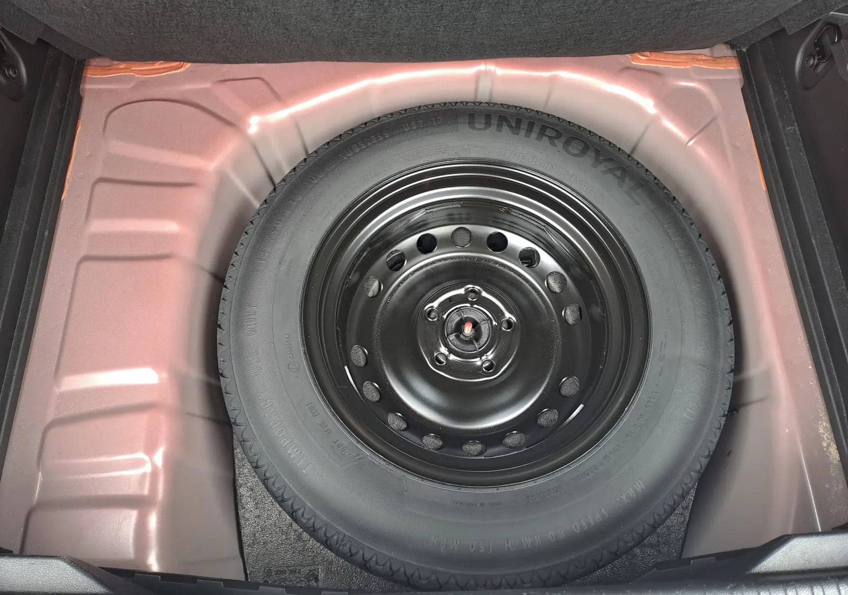 Vue plongeante sur la roue de secours noire dans le coffre rouge flamme métal du Renault Captur TCE 90CH TECHNO 2024.