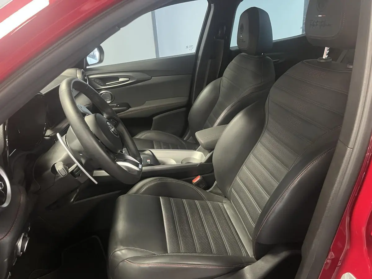 Intérieur côté conducteur de l'Alfa Romeo Tonale rouge 2024, sièges sport cuir noir avec surpiqûres rouges et volant sport.