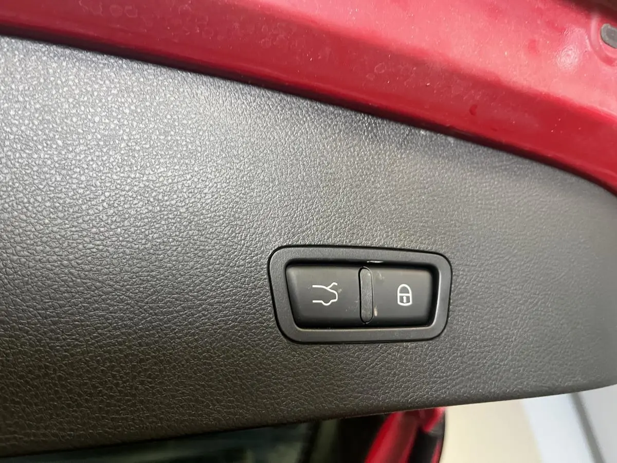 Gros plan sur le bouton de fermeture du coffre, entouré de plastique noir, sur un Alfa Romeo Tonale rouge.