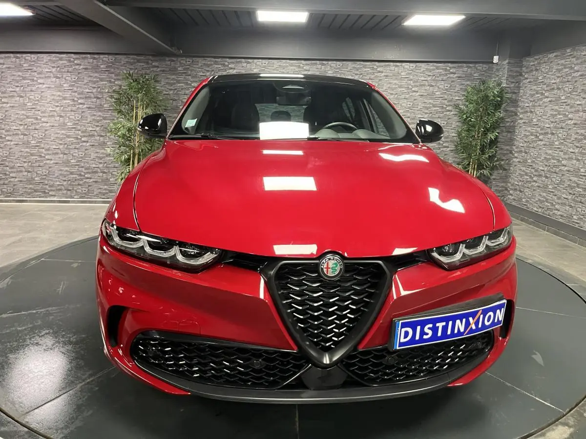 Vue frontale d'une Alfa Romeo Tonale rouge avec calandre noire et phares LED distinctifs dans un showroom.