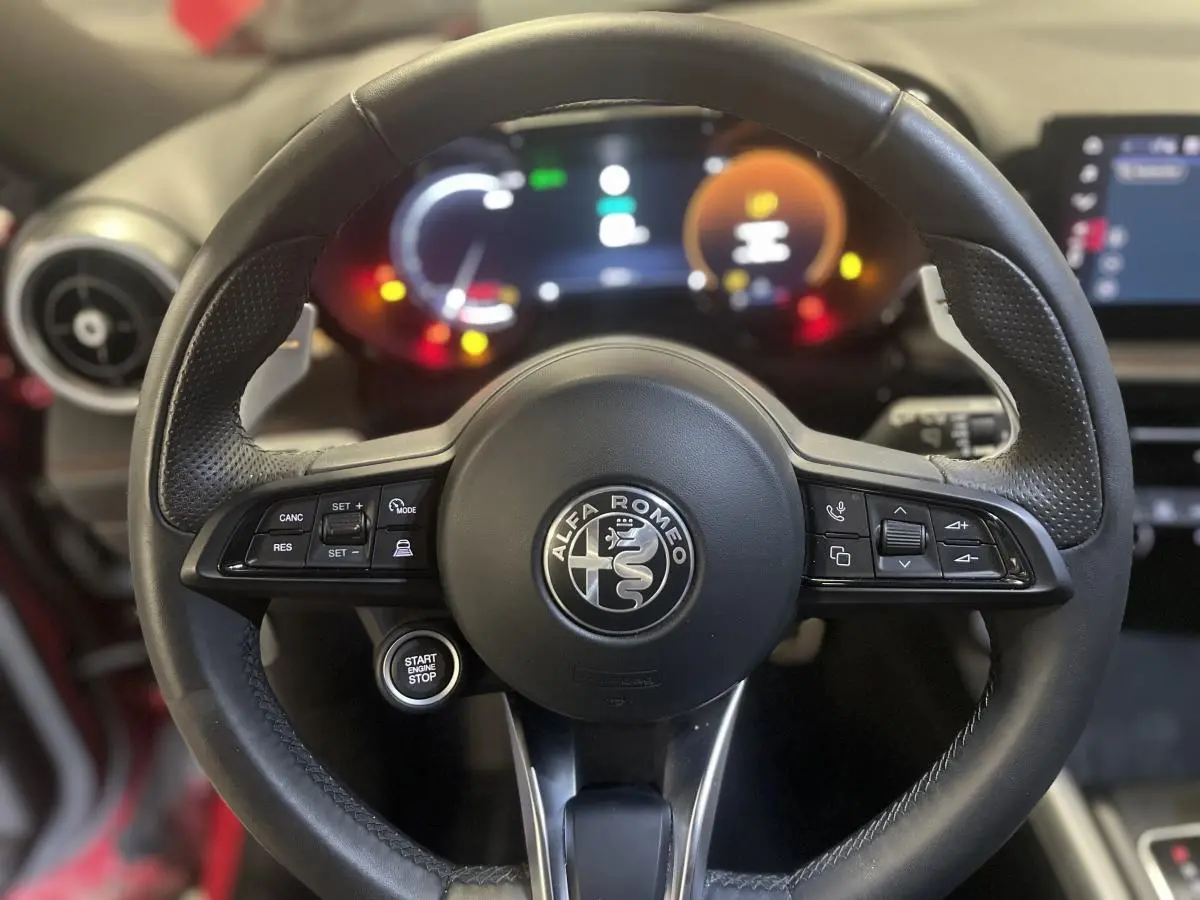Volant sport en cuir noir avec logo Alfa Romeo, bouton start/stop, et tableau de bord digital lumineux.