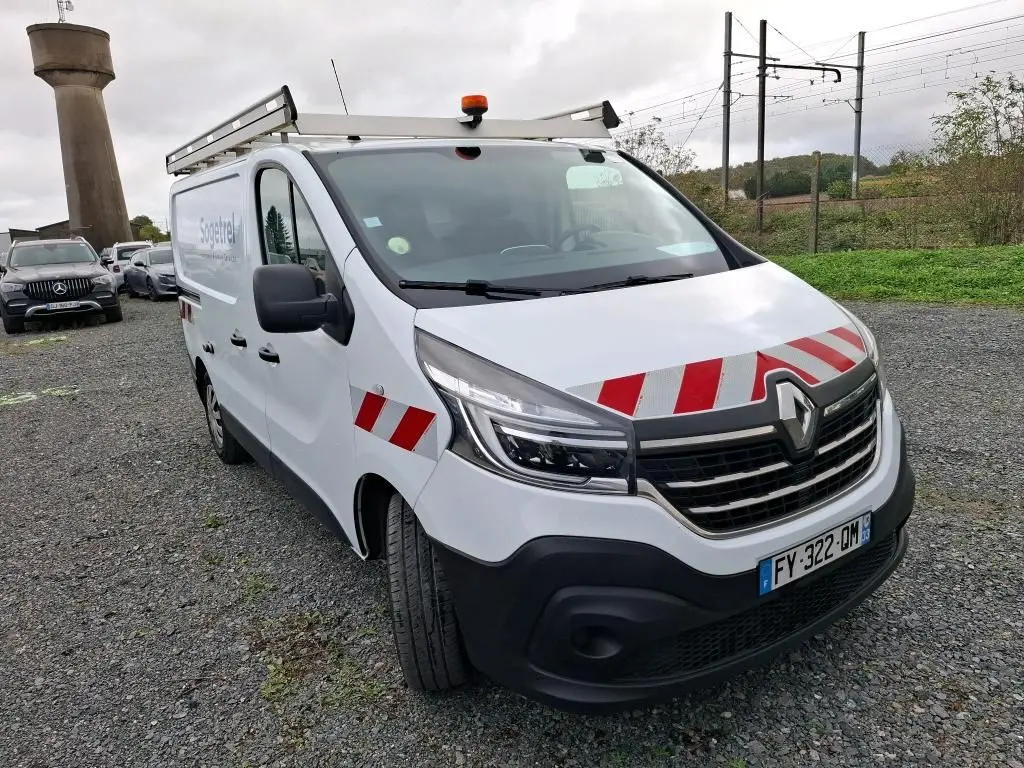 Renault Trafic Fourgon blanc en 3/4 avant droit avec bandes rouges réfléchissantes et galerie de toit.