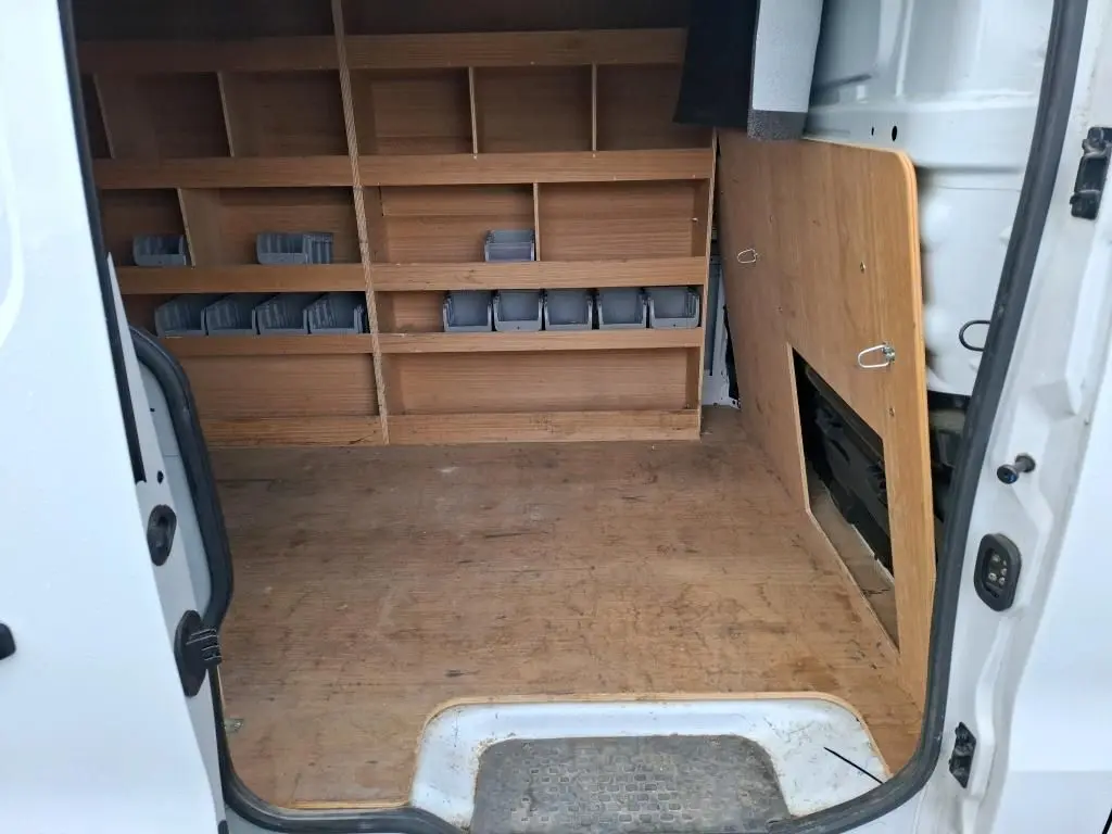 Vue intérieure arrière du Renault Trafic Fourgon blanc, montrant l'aménagement bois avec étagères et rangements intégrés.