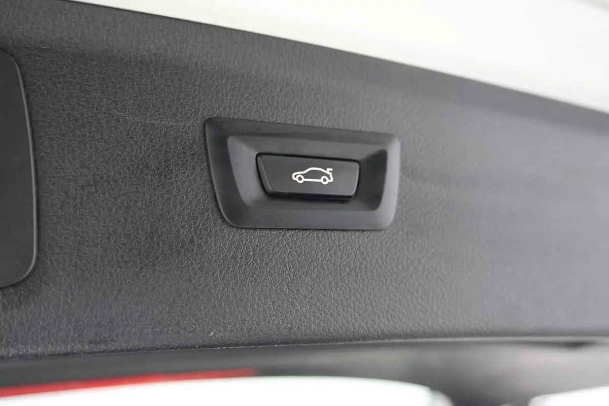 Gros plan sur le bouton d'ouverture électrique du hayon intérieur d'une BMW Série 2 Active Tourer blanche.