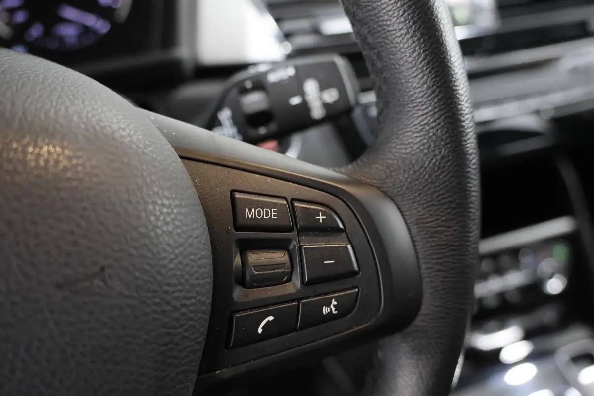 Gros plan sur les commandes multifonctions noires du volant en cuir de la BMW Série 2 Active Tourer 216d.