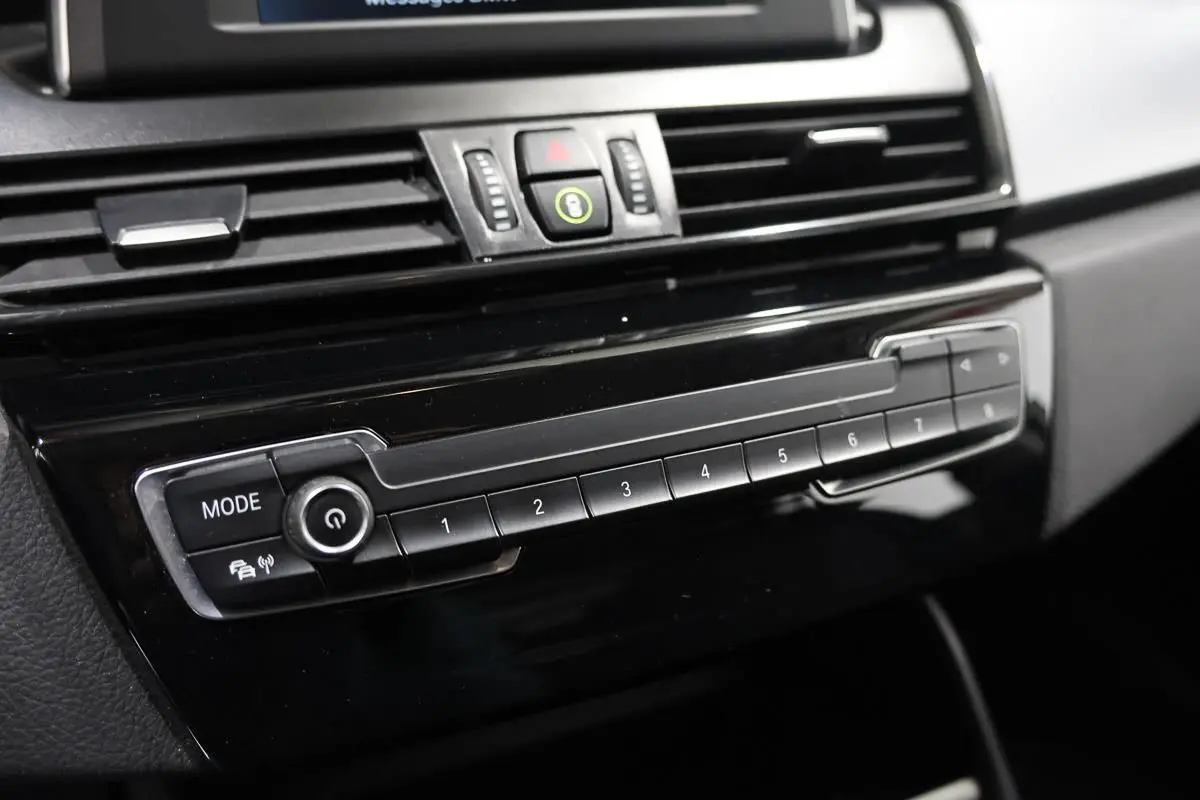 Gros plan sur la console centrale noire de la BMW Série 2 Active Tourer 216d, mettant en valeur les boutons de commande et l'écran supérieur.