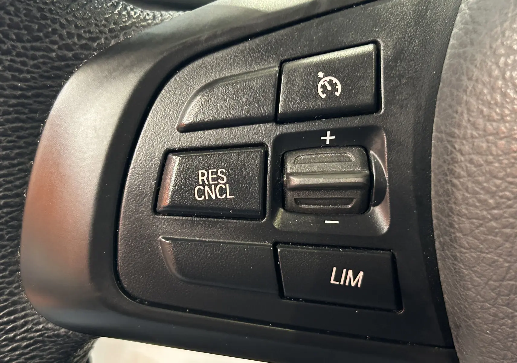 Gros plan sur les commandes du régulateur de vitesse au volant d’une BMW Série 2 Active Tourer blanche.