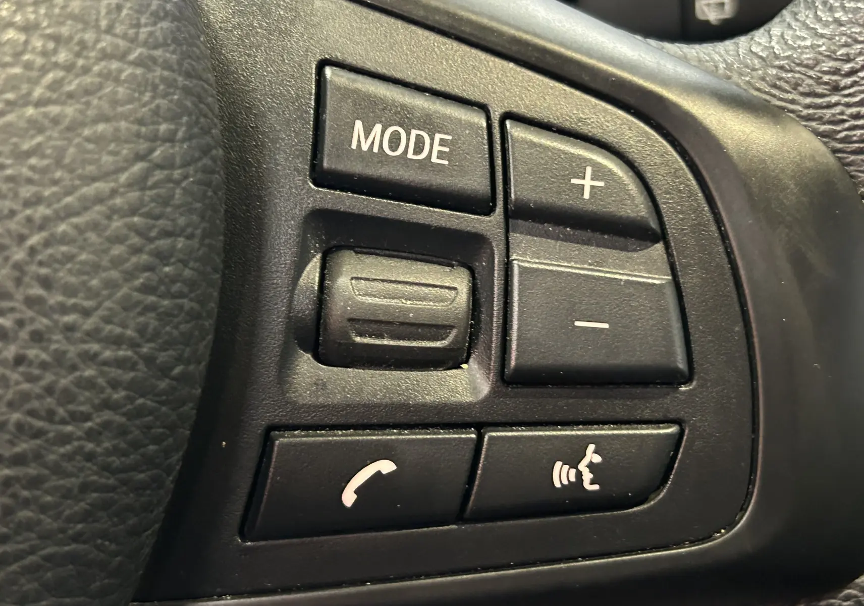 Gros plan sur les commandes noires du volant côté gauche de la BMW Série 2 Active Tourer blanche, boutons mode et téléphone.
