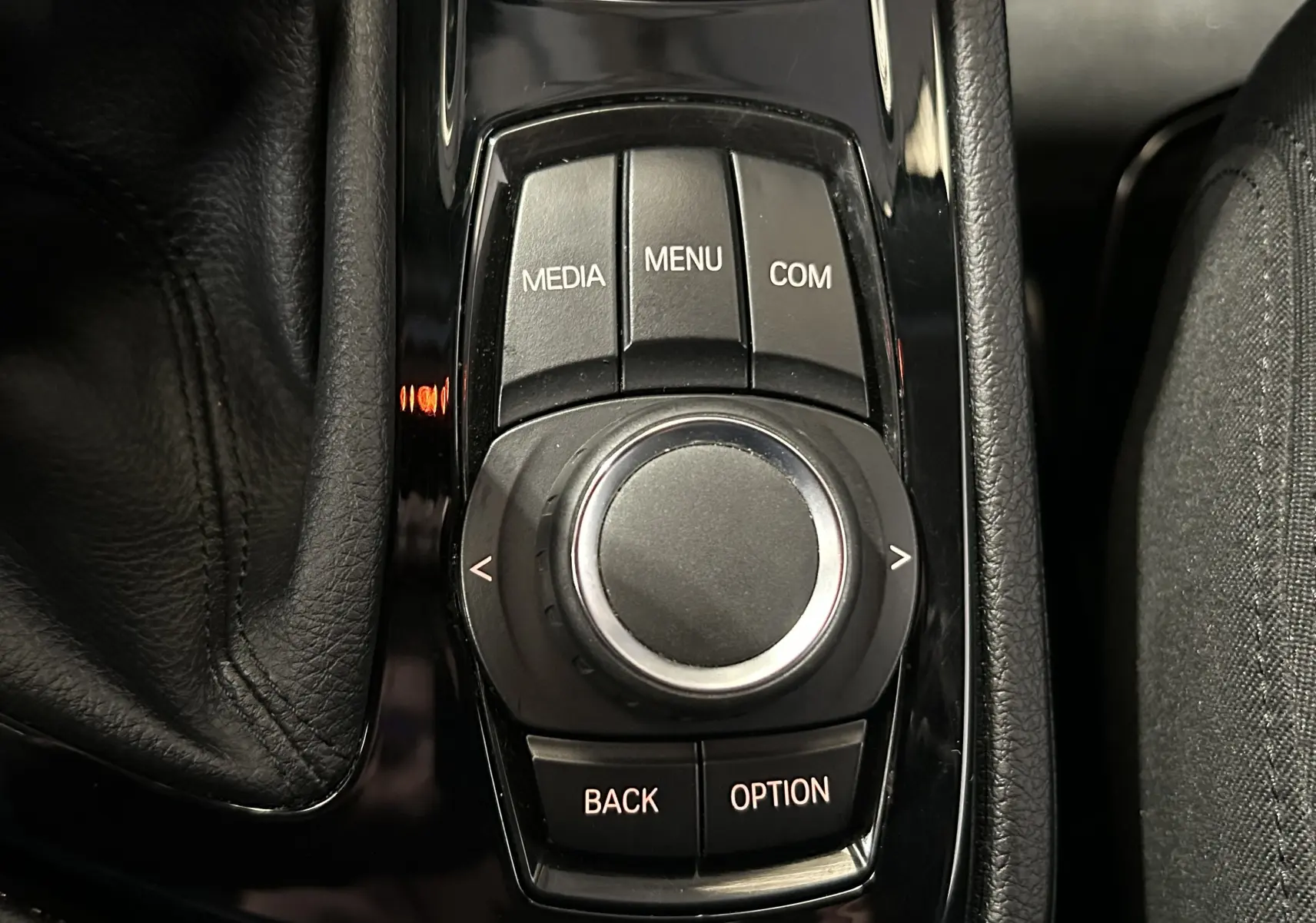 Gros plan sur la molette de commande centrale noire brillante de la BMW Série 2 Active Tourer blanche, entourée de boutons fonctionnels.