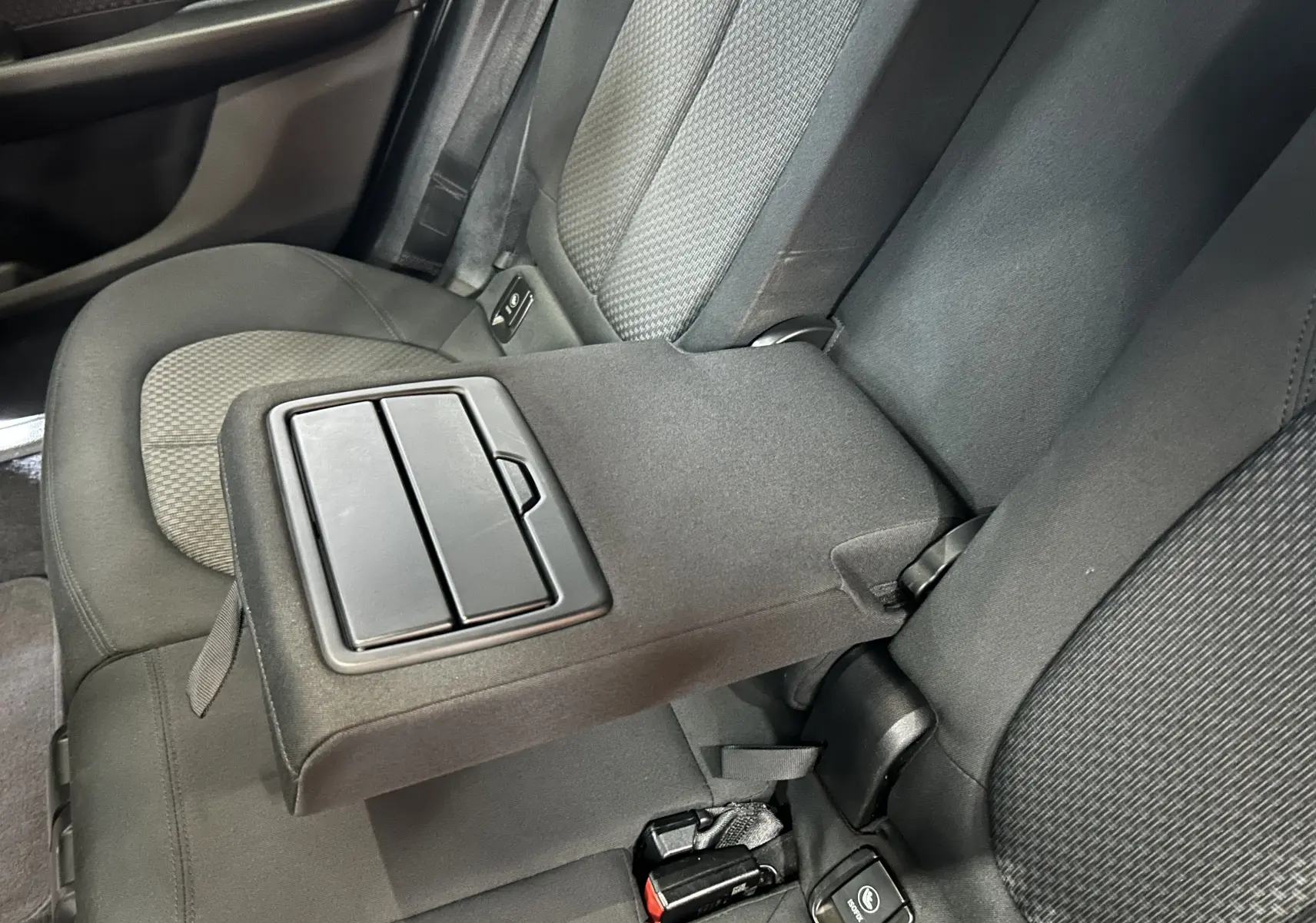 Vue intérieure des sièges arrière noirs d'une BMW Série 2 Active Tourer 216d avec accoudoir central relevé.