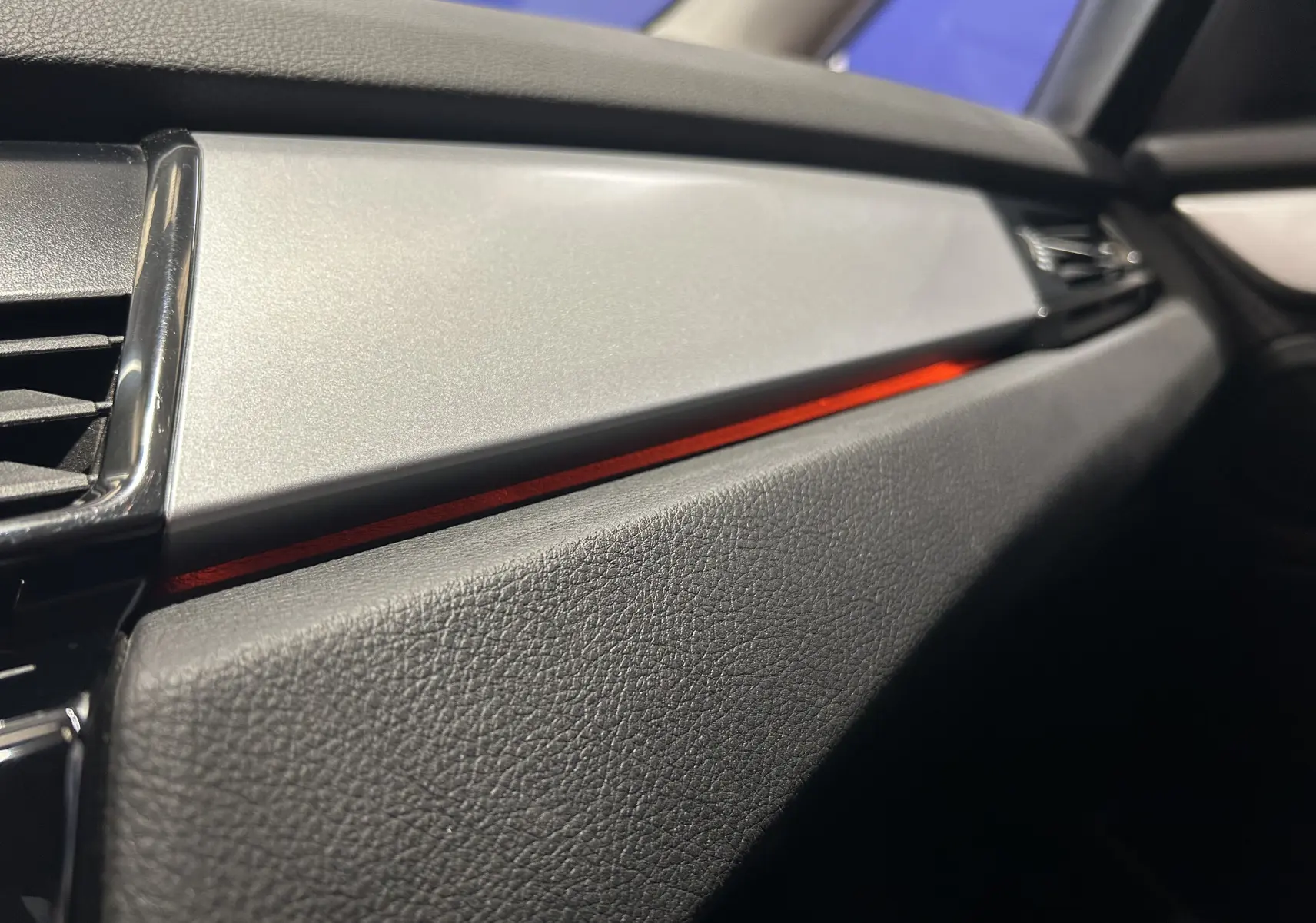 Détail de la planche de bord côté passager de la BMW Série 2 Active Tourer 216d 2021 avec bandeau décoratif rouge et finition noire texturée.