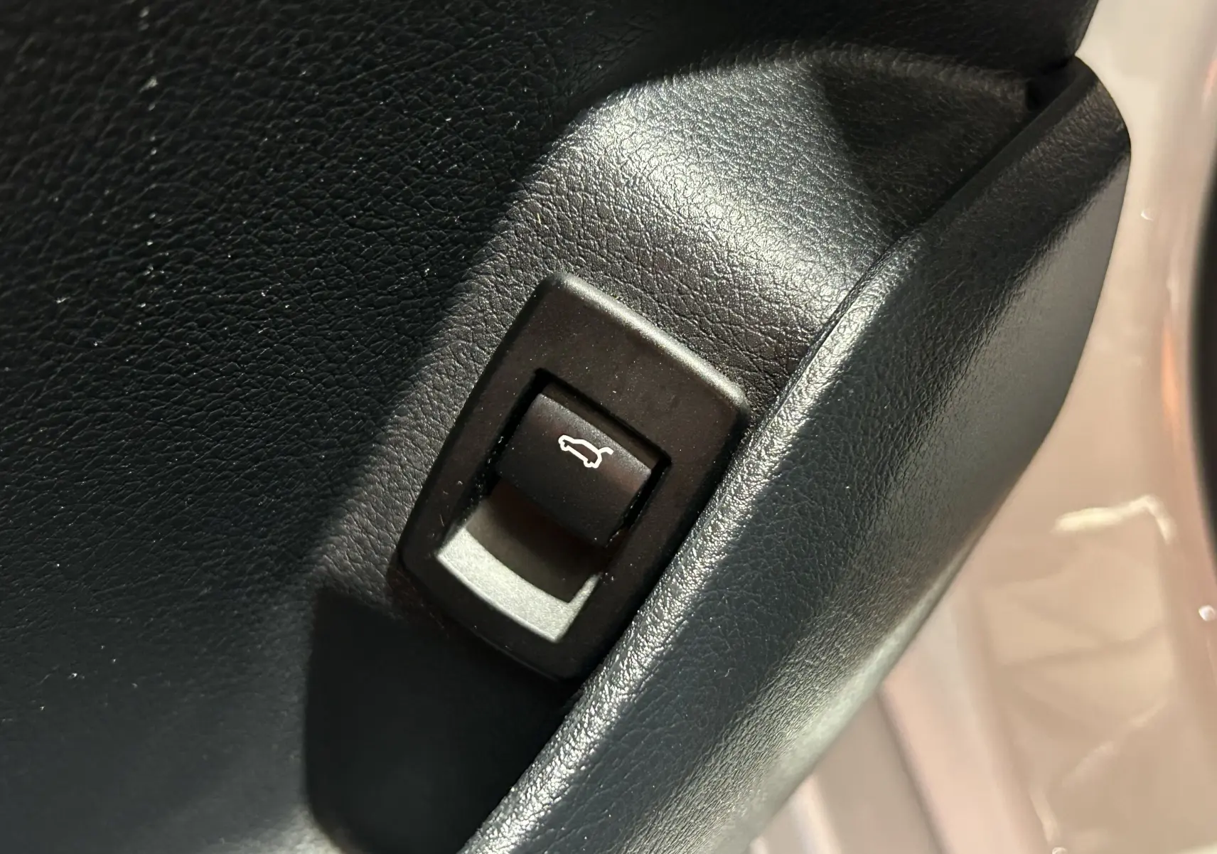 Gros plan sur le bouton d'ouverture du coffre noir dans l'habitacle d'une BMW Série 2 Active Tourer blanc.