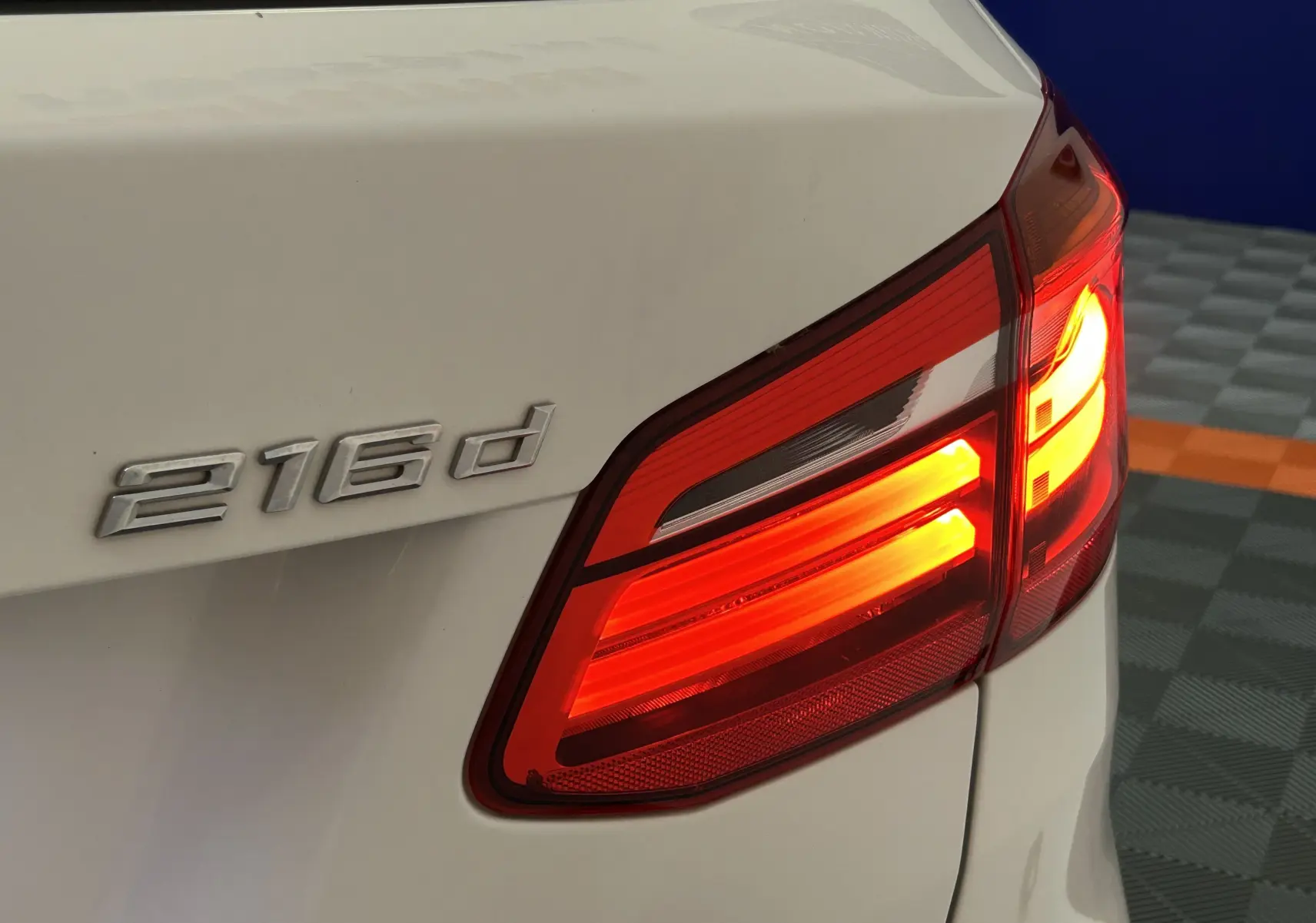 Gros plan sur le feu arrière droit allumé et l’inscription 216d sur la malle arrière d’une BMW Série 2 Active Tourer blanche.