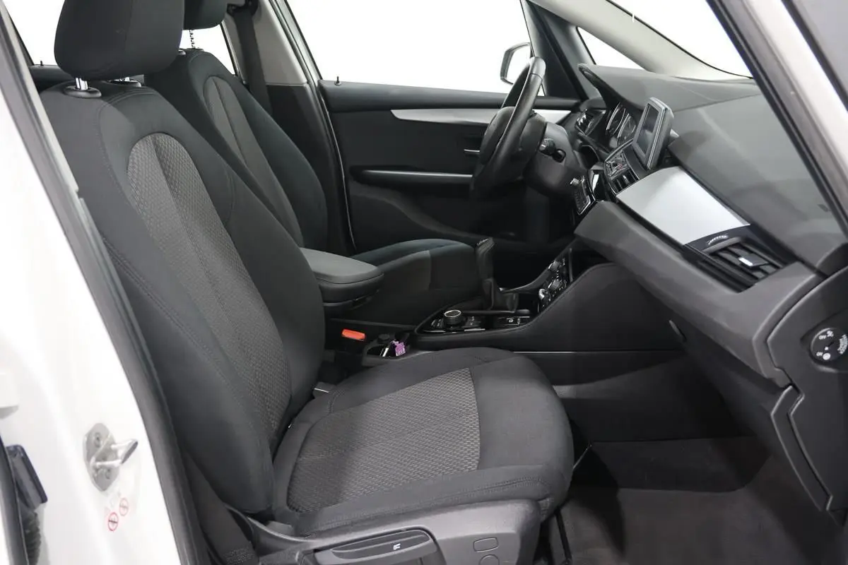 Vue intérieure côté conducteur de la BMW Série 2 Active Tourer blanche, sièges tissu noirs avec volant cuir et console centrale.