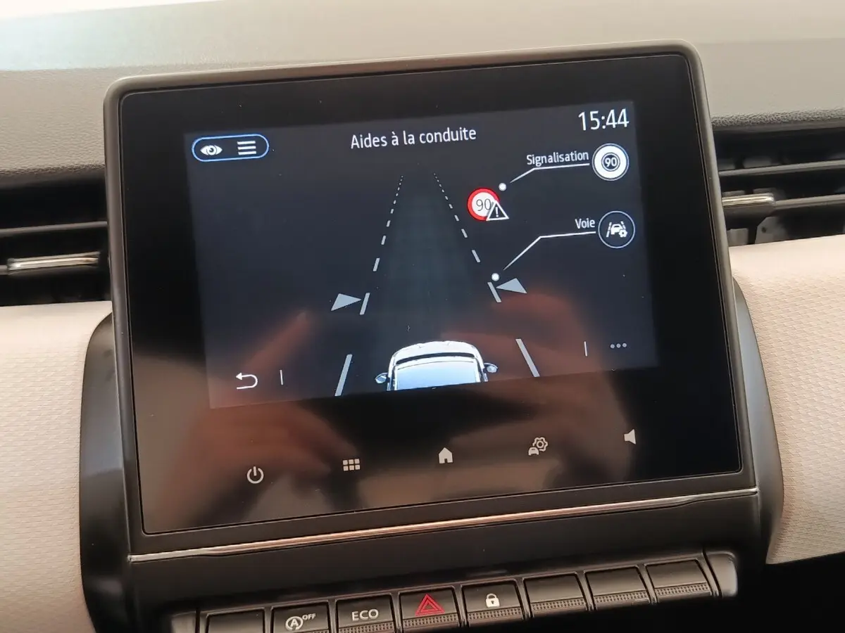 Écran tactile central de la Renault Clio blanc montrant l’aide à la conduite avec alertes de signalisation et voie.