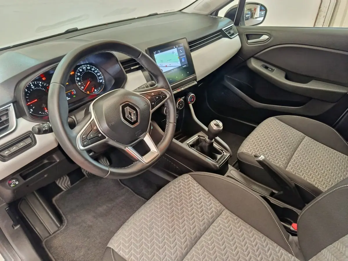 Vue intérieure avant droite de la Renault Clio 2023, volant cuir, écran tactile central et sièges tissu gris.