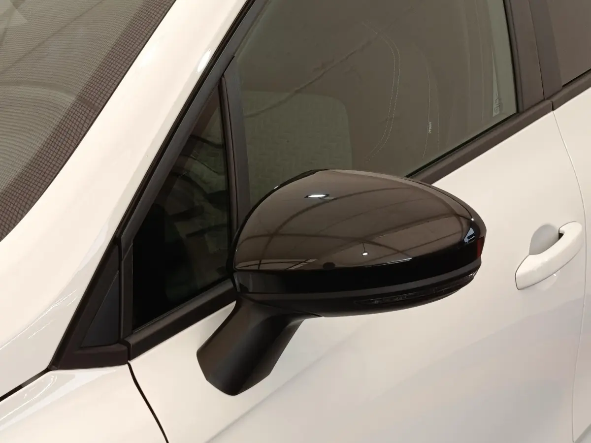 Rétroviseur droit noir brillant sur Renault Clio blanc, vue rapprochée côté avant droit avec porte visible.