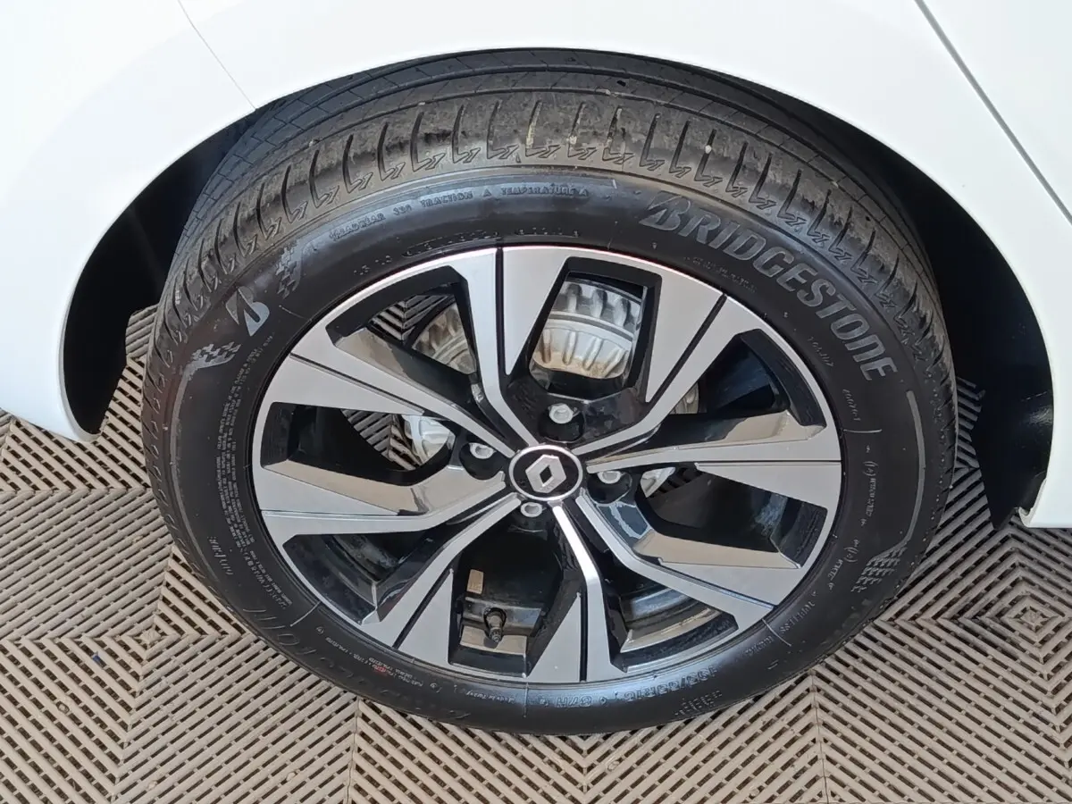 Gros plan sur la roue avant droite d’une Renault Clio blanche, jante alliage bicolore avec logo Renault central.