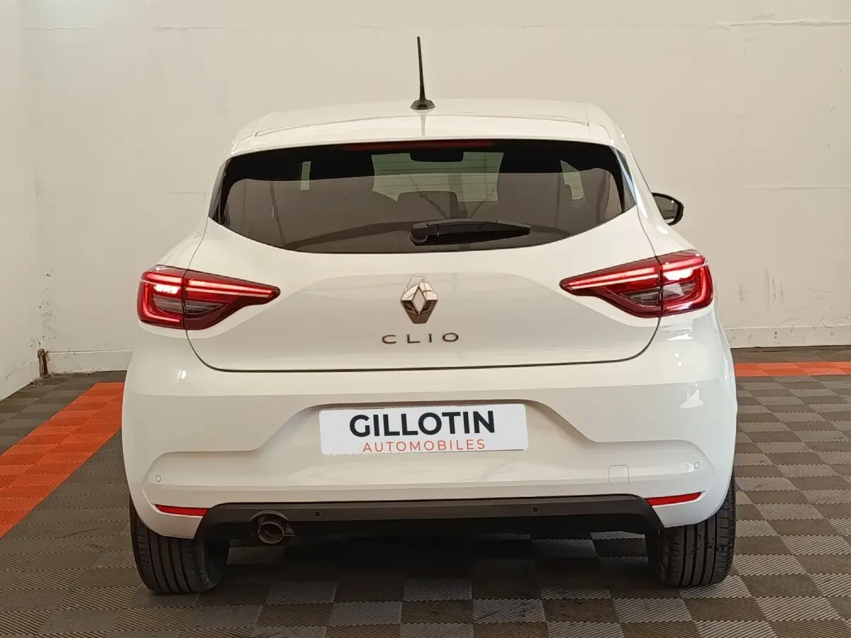 Vue arrière d'une Renault Clio blanche 2023 avec feux LED allumés et logo Renault visible au centre.