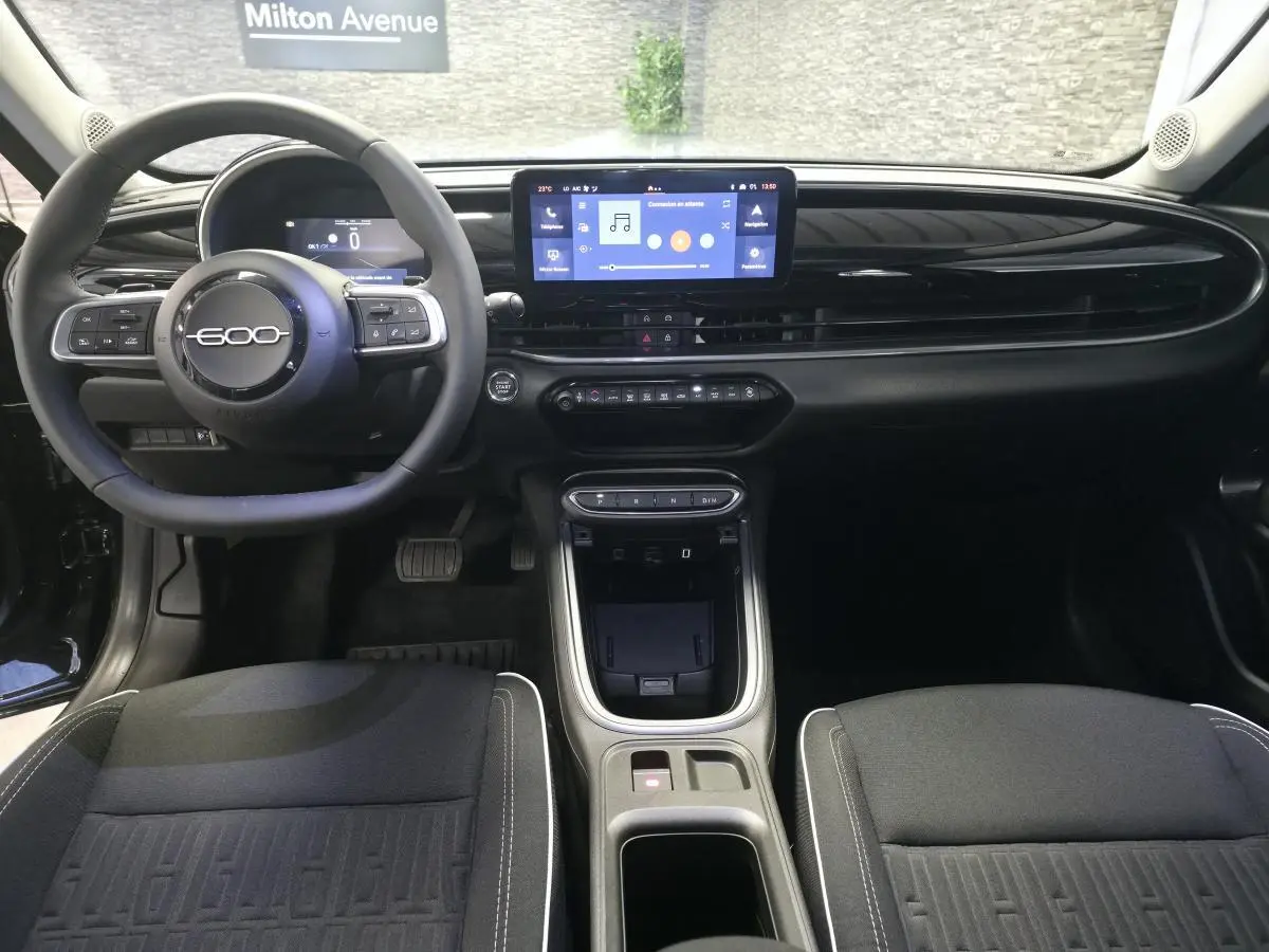 Vue intérieure avant du tableau de bord noir brillant et volant du Fiat 600 Hybrid avec écran tactile central.