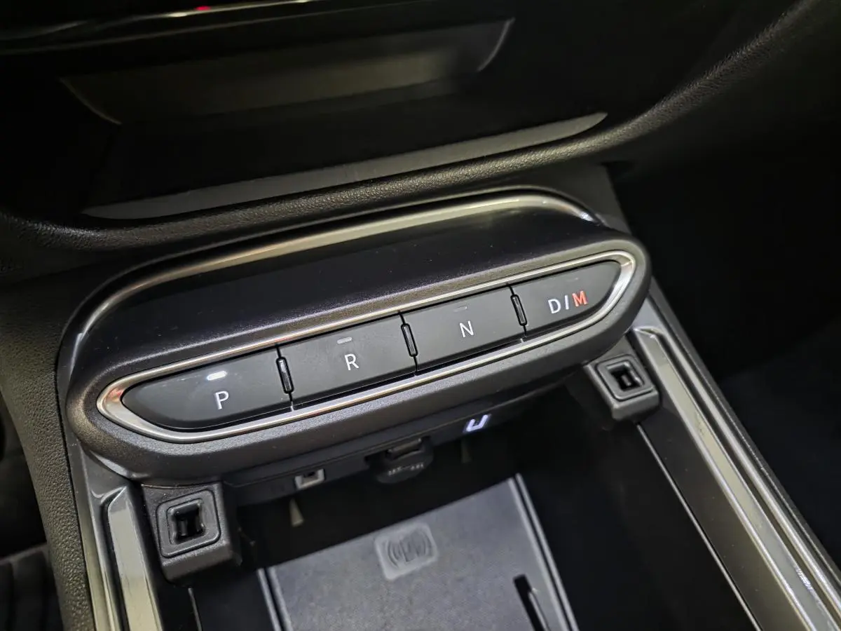 Gros plan sur la console centrale noire du Fiat 600 Hybrid 2025, avec boutons de boîte auto P, R, N, D/M et chargeur induction.