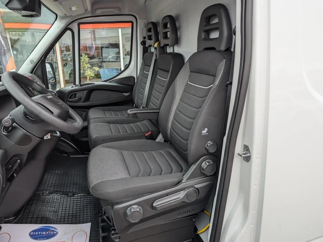 Vue intérieure côté conducteur du fourgon blanc Iveco Daily 35S16 avec sièges tissu gris et tableau de bord noir.