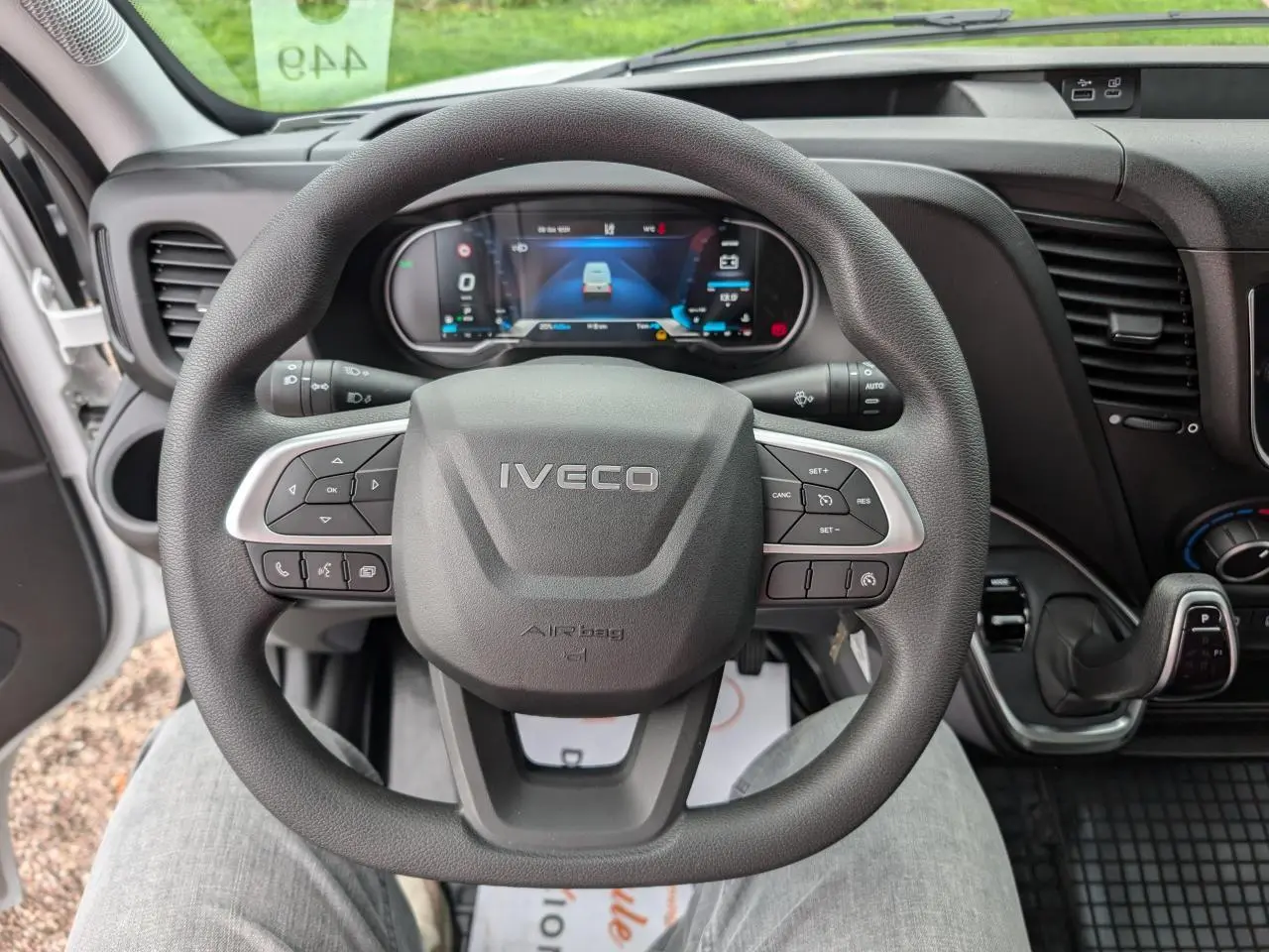 Vue rapprochée du volant IVECO Daily 35S16 avec commandes intégrées et tableau de bord digital en arrière-plan.