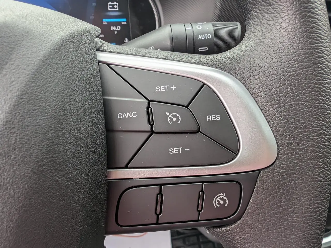 Gros plan sur les commandes du régulateur de vitesse au volant du Iveco Daily blanc, avec affichage digital en arrière-plan.