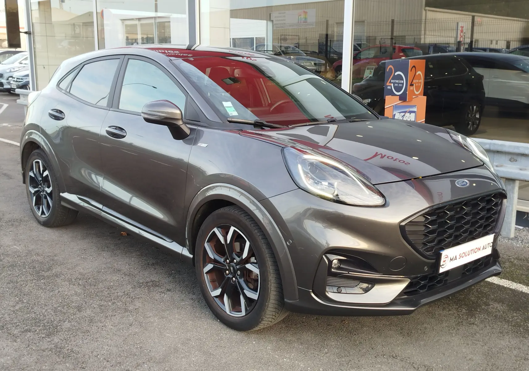 Ford Puma 1.0 EcoBoost gris métallisé en 3/4 avant droit, avec jantes alliage et calandre noire distinctive.